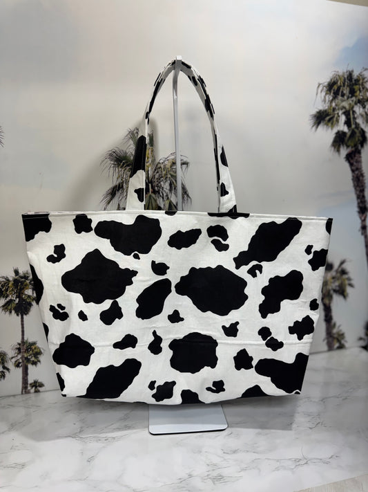 Cow print tote bag on a marble surface with palm tree background