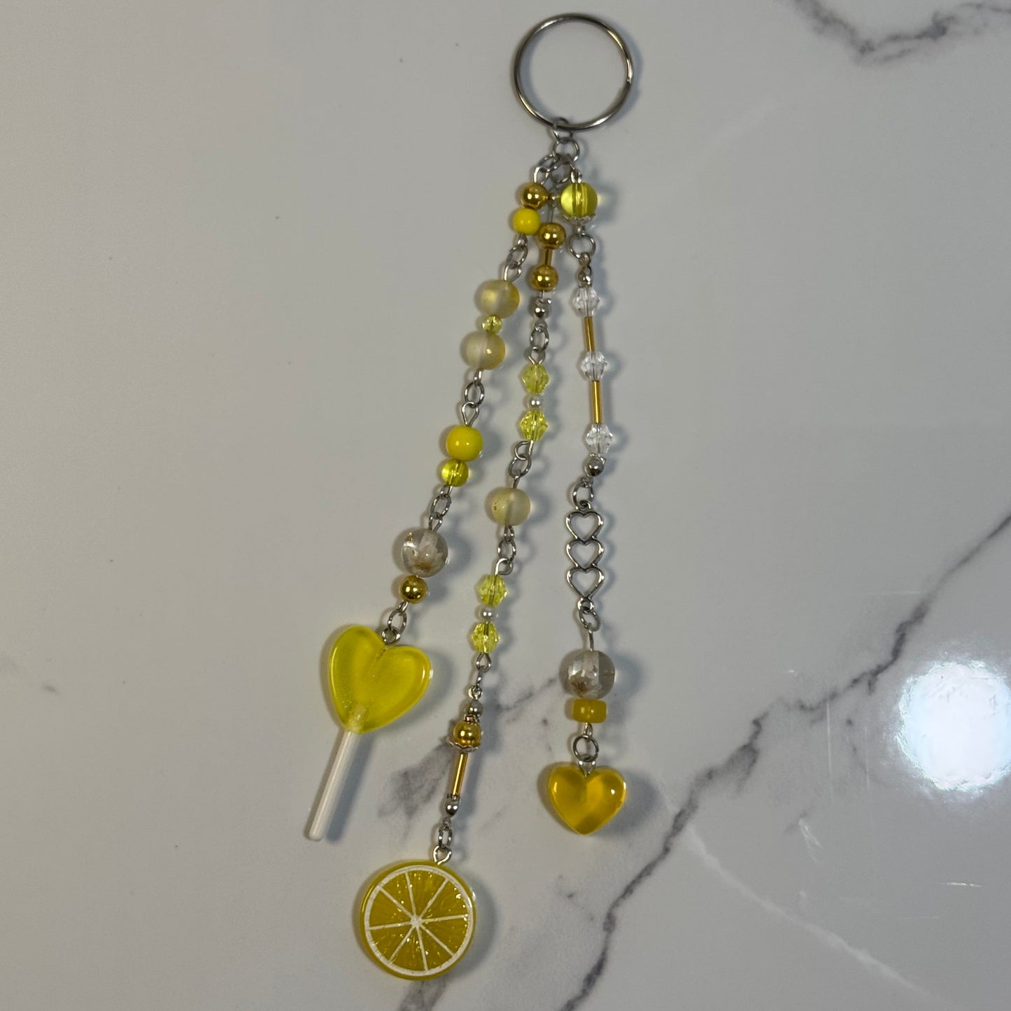Keychain with yellow heart, lollipop, and lemon slice charms on a marble surface