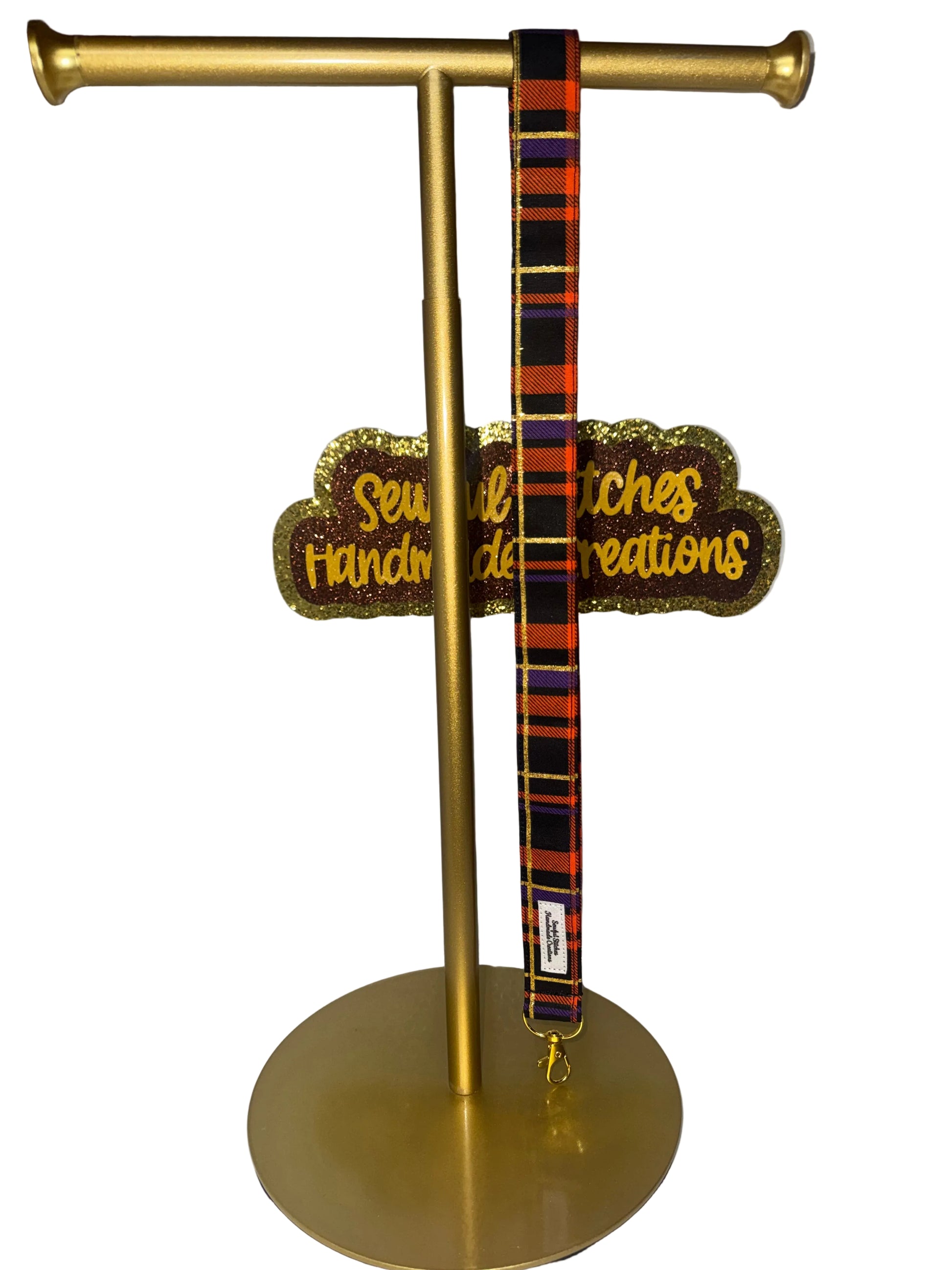 A gold metal display stand holding a lanyard with black, orange, and red plaid pattern and thin gold stripes.