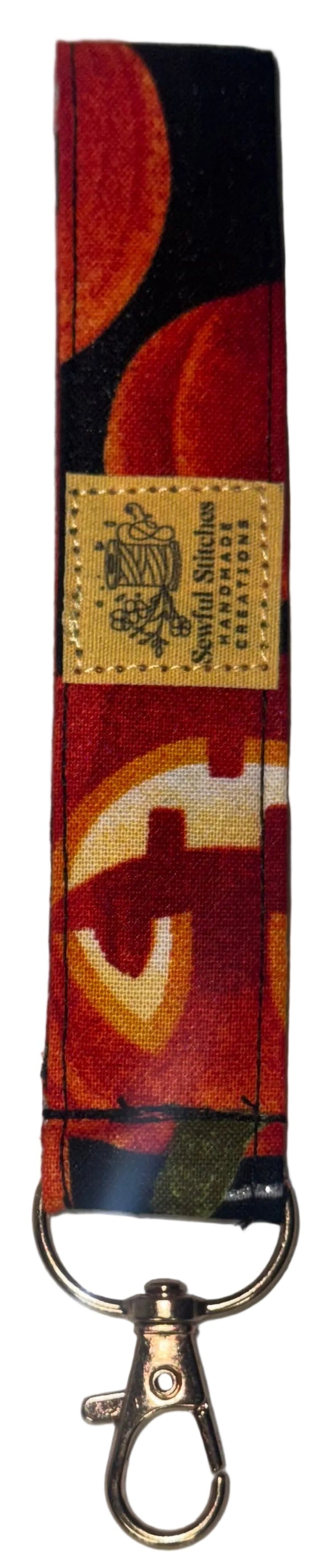 A fabric keychain strap featuring a red, orange, and black abstract pumpkin pattern with a gold-colored metal swivel clasp at the bottom, displayed on a white surface.